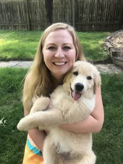 Dr.Andrea holding a fluffy golden retriever puppy, both looking happy, with a blurred green backyard setting.